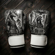 Black and white boxing gloves featuring the Egyptian jackal god Anubis, pyramids, an obelisk, a falcon-headed Pharaoh, ancient temples, and a soaring eagle art design for combat sports training.