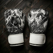 Black and white boxing gloves featuring a medieval knight with a sword and shield on a battlefield, and a fantasy dragon perched over an ancient castle under a stormy sky for combat sports training.