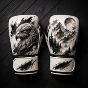 White and black boxing gloves featuring a fierce eagle portrait, pine forest, mountain peaks, and full moon ink wash art design for combat sports training.