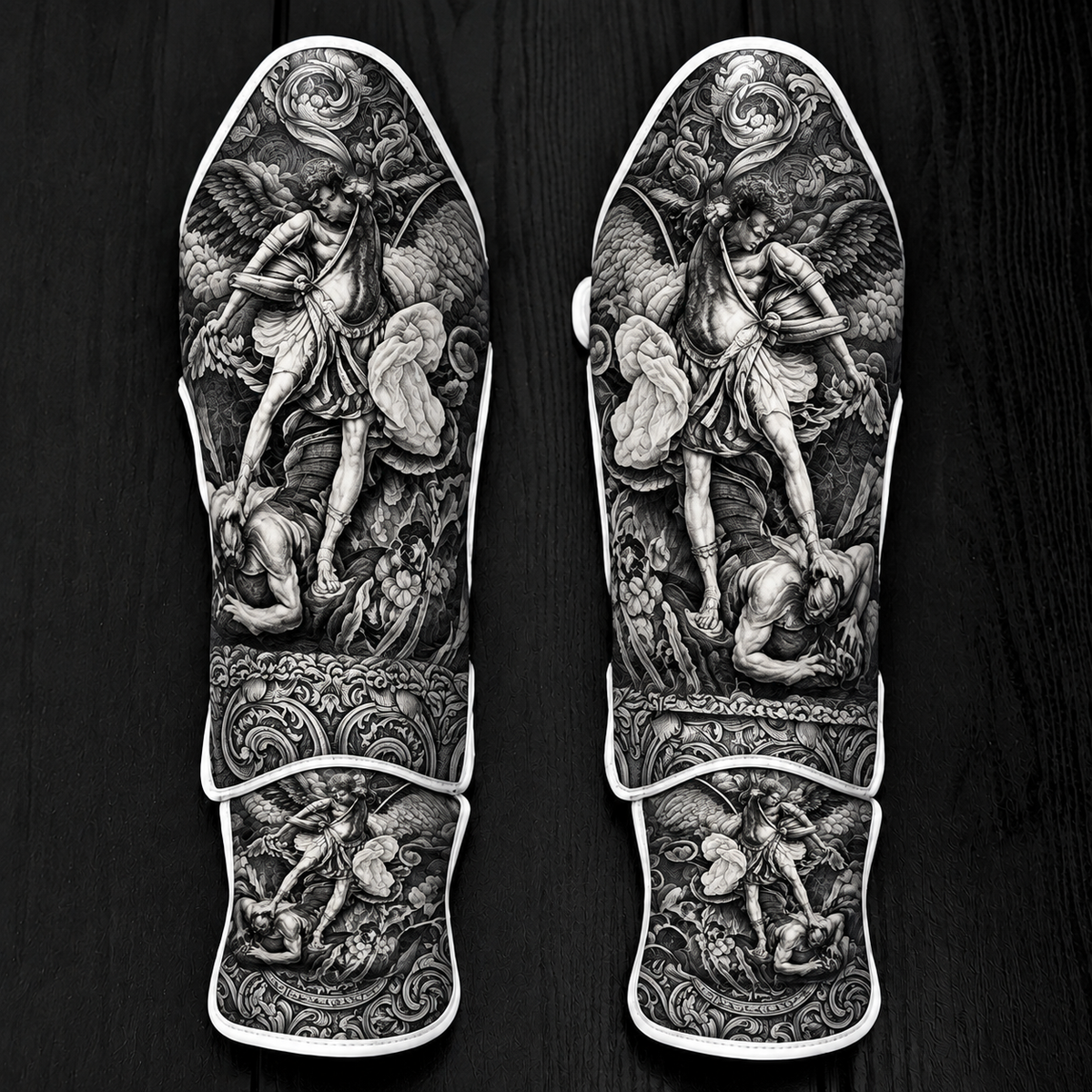 Fiest Gloves custom black-and-grey kickboxing and MMA shin guards featuring detailed baroque Renaissance artwork of Archangel Michael defeating a fallen figure, complemented by intricate floral and scrollwork patterns