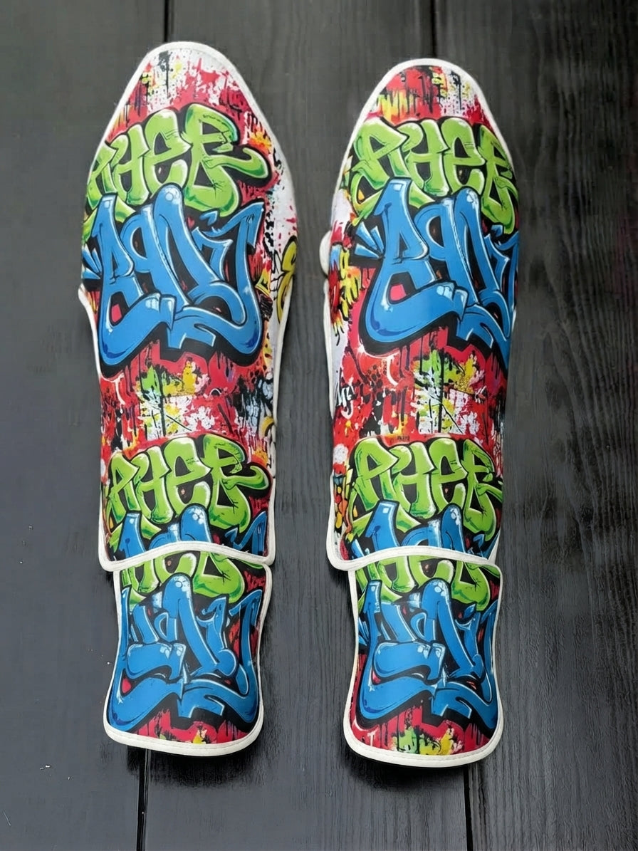 Fiest Gloves custom kickboxing and MMA shin guards featuring vibrant urban graffiti art with blue, green, and red paint-splatter sublimation print layout.