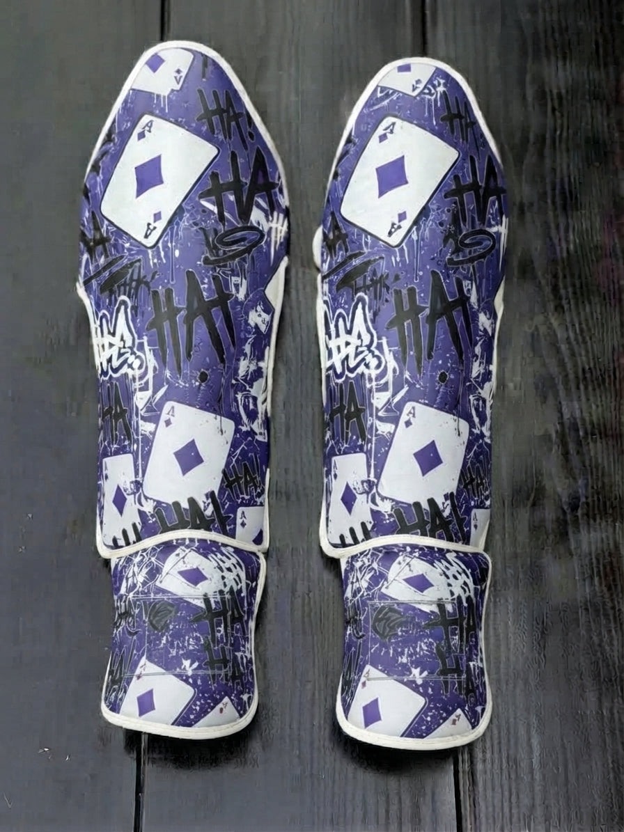 Fiest Gloves custom villain-themed kickboxing and MMA shin guards featuring a purple background, repeating "HA HA" graffiti typography, and Ace of Diamonds playing card motifs
