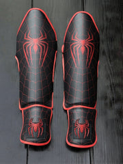 Fiest Gloves custom superhero-themed kickboxing and MMA shin guards featuring a black base with red spider web patterns and prominent spider emblem logos