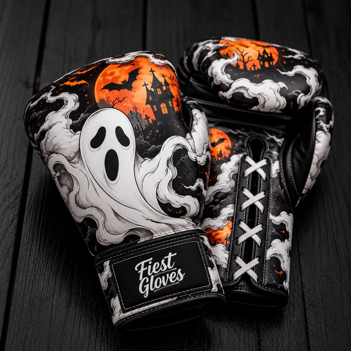 Pair of Fiest Gloves boxing gloves featuring a spooky Halloween ghost design, haunted castle silhouette, bats, and full moon background on dark wooden background.