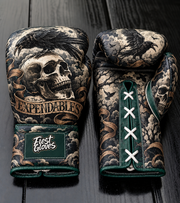 Fiest Gloves featuring a dark raven perched on a skull with a gold banner reading 'The EXPENDABLES', cloudy sky background, dark green trim, and white laces on a dark wood surface.   