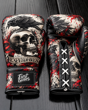 Fiest Gloves featuring a black raven perched on a skull with a banner reading 'The EXPENDABLES', red splatter accents, and white laces on a dark wooden background.   