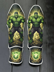 Custom Hulk superhero design with muscular green physique, gamma energy veins, destroyed ground background, and glowing cracked green stone emblem soccer shin guards displayed on a dark surface.