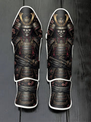 Custom Japanese samurai design with traditional ornate kabuto helmet, menacing mempo mask, layered armor, crossed katanas, and pink cherry blossom floral background soccer shin guards displayed on a dark surface.