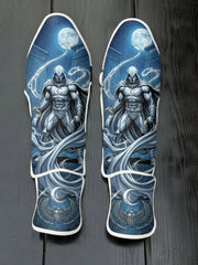 Custom Moon Knight superhero design with white hooded cloak, crescent darts, full moon, Egyptian hieroglyphics, and winged scarab emblem soccer shin guards displayed on a dark surface.