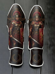 Custom Roman centurion design with red plumed helmet, scale armor, gladius sword, shield with golden eagle wings, and laurel wreath emblem soccer shin guards displayed on a dark surface.