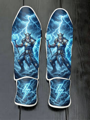 Custom Thor superhero design with horned helmet, glowing hammer, blue lightning bolts, stormy clouds, and lightning bolt emblem soccer shin guards displayed on a dark surface.