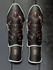 Custom Viking warrior design with fur armor, bloody battle axes, Norse runic circular backdrop, and metallic shield emblem soccer shin guards displayed on a dark surface.