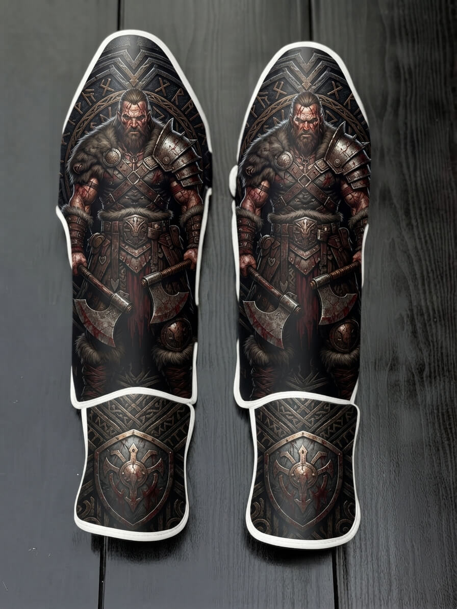 Custom Viking warrior design with fur armor, bloody battle axes, Norse runic circular backdrop, and metallic shield emblem soccer shin guards displayed on a dark surface.