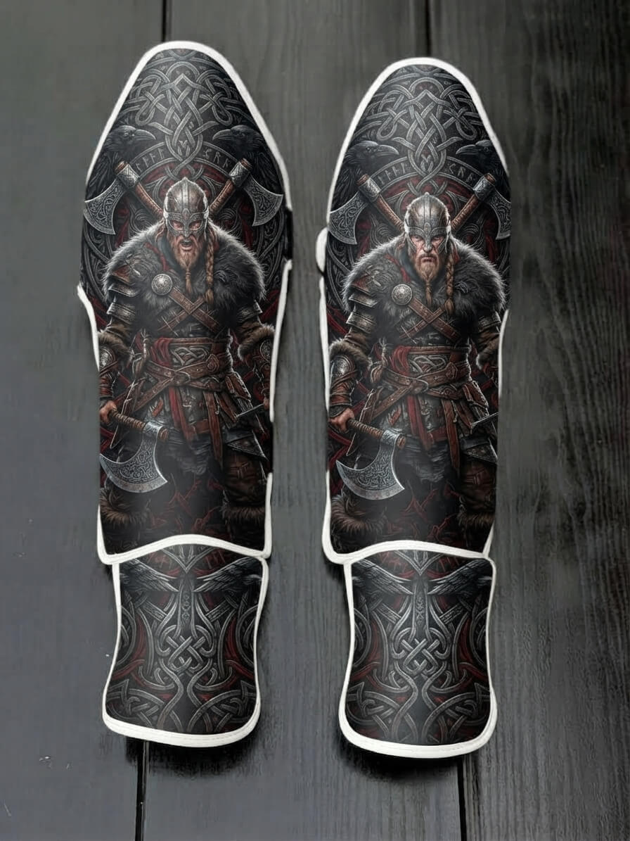 Custom Viking warrior design with horned or metal helm, fur armor, battle axes, intricate Celtic knotwork background with ravens, and Norse shield emblem soccer shin guards displayed on a dark surface.